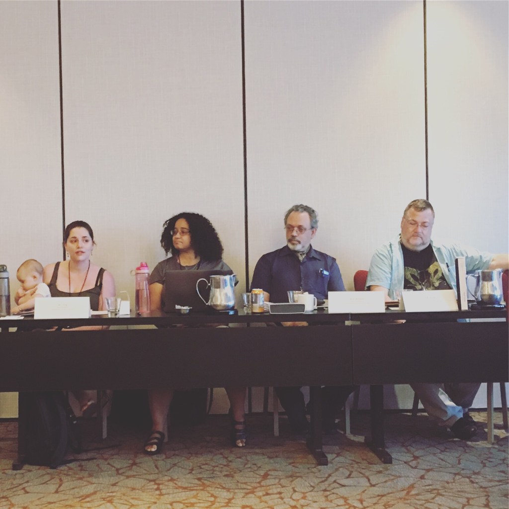 A table in a hotel conference room with 4 people. Left to right: me, a dark-haired white woman with a white baby on my lap, Kathleen Kayembe, a biracial woman with light brown skin and curly black hair, Walter Williams, a gray-haired white man with a goatee, and Richard Wood, a gray-haired white man
